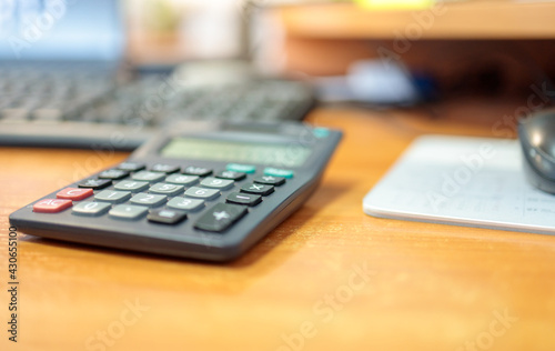 calculator is on the table against background of the keyboard and mouse, background is blurred