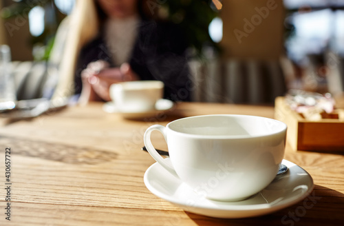 Cup of coffee on the table. Woman typing text message on smart phone in a cafe. Young woman sitting at a table with a coffee using mobile phone. Coffee break. Blurred image, ..selective focus