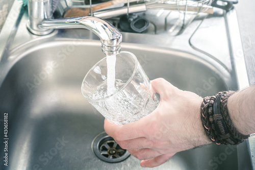 Man Holding A Drinking Glass Over Kitchen Sink Filling It With Water Pouring From Faucet