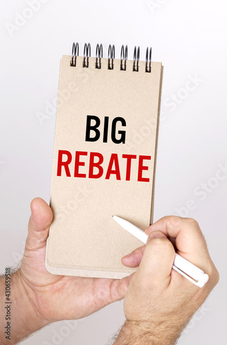 A man holds a pen and a bolknot in his hands with the inscription - Big Rebate