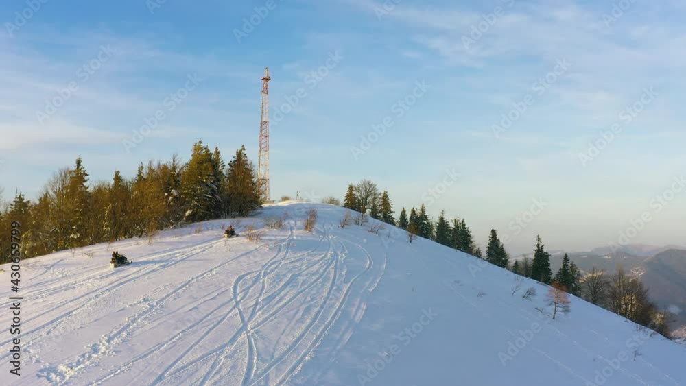 A warmly dressed man sitting on a snowmobile quickly rides along a snow-covered narrow path, evergreen spruce plants to a high honeycomb tower against the backdrop of a fabulous sky A warmly dressed man sitting on a snowmobile quickly rides along a snow-covered narrow path, evergreen spruce plants to a high honeycomb tower against the backdrop of a fabulous sky