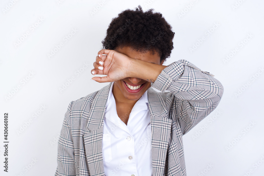 African American businesswoman with curly bushy hair wears formal clothes over white background covering eyes with arm smiling cheerful and funny. Blind concept. African American businesswoman with curly bushy hair wears formal clothes over white background covering eyes with arm smiling cheerful and funny. Blind concept.