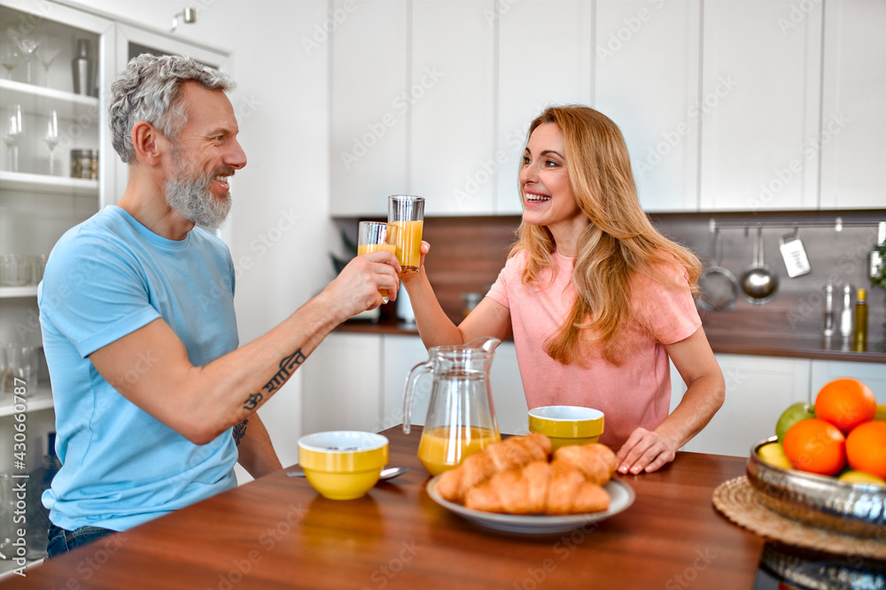 Mature couple have breakfast in the kitchen early in the morning and have a good time. A married couple have breakfast with juice and croissants. Mature couple have breakfast in the kitchen early in the morning and have a good time. A married couple have breakfast with juice and croissants.