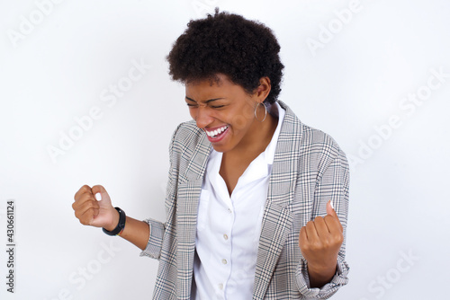 African American businesswoman with curly bushy hair wears  formal clothes over white background very happy and excited doing winner gesture with arms raised, smiling and screaming for success. © Roquillo