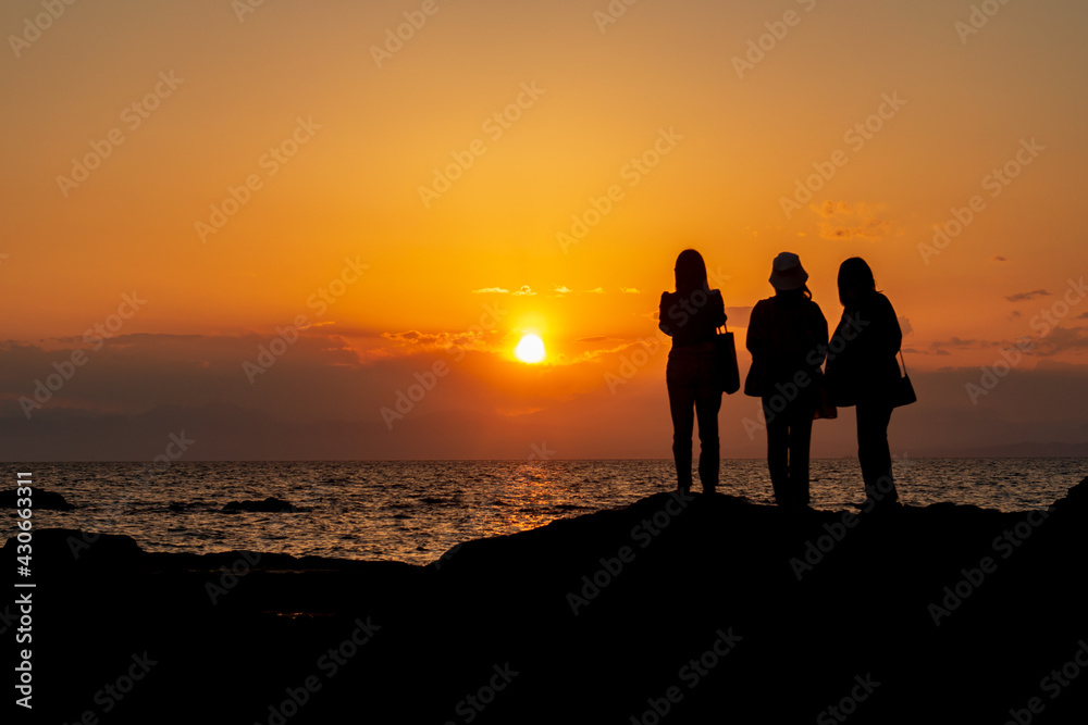 海に沈む夕日を眺める3人の若い女性のシルエット　秋谷海岸　立石公園　梵天の鼻