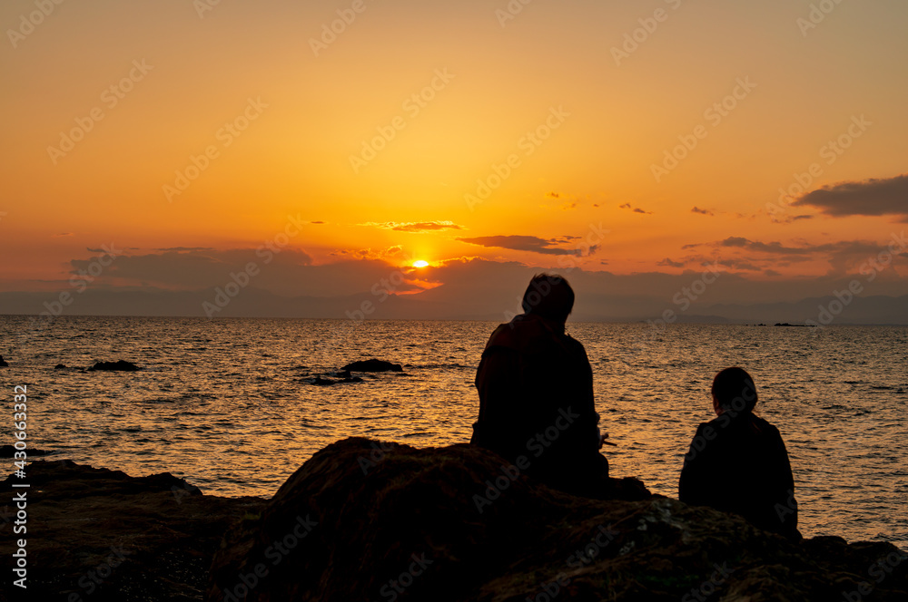 海に沈む夕日を眺めるカップルのシルエット　秋谷海岸　立石公園　梵天の鼻