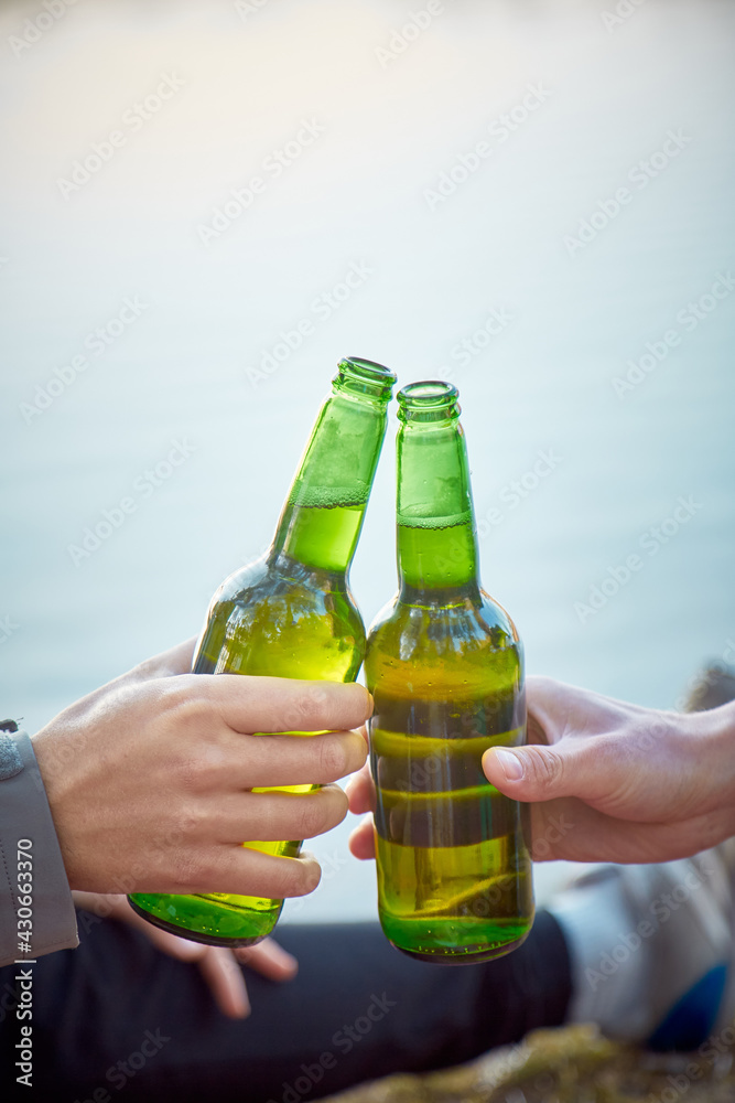2 bottles of beer in frount of water in the hands of men. The concept of spending time in nature. Close up