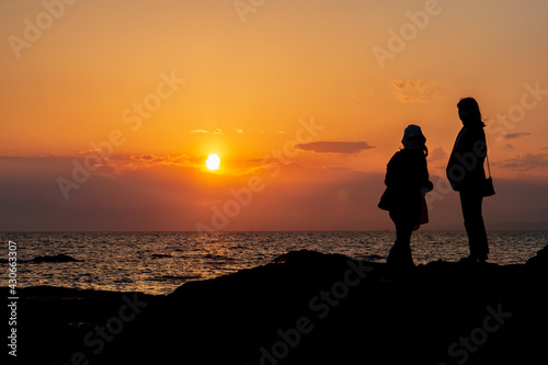 海に沈む夕日を眺める2人の若い女性のシルエット 秋谷海岸 立石公園 梵天の鼻
