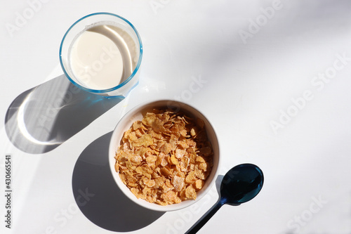 Bowl of cereal and glass of milk on white background. Healthy breakfast with cornflakes and milk. Top view, copy space. Hard light, shadow