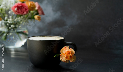 Dark cup with coffee on a dark background, Nearby is a bouquet of flowers