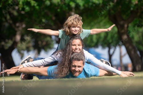 Cute family portrait. Portrait of a happy smiling family relaxing in park. Family lying on grass in park. Fly concept, little boy is sitting pickaback while imitating the flight.