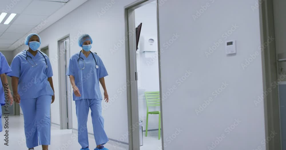 Diverse female surgeons wearing face masks walking in hospital corridor Diverse female surgeons wearing face masks walking in hospital corridor