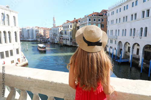 Holidays in Venice. Back view of beautiful girl in red dress enjoying view of Grand Canal from Rialto Bridge in Venice, Italy.