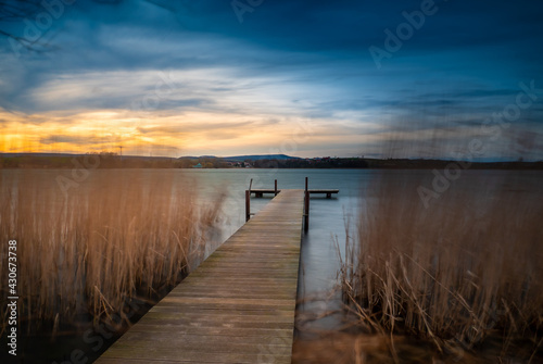 Beautiful shot of a wooden dock in between tall grasses on a river during sunset