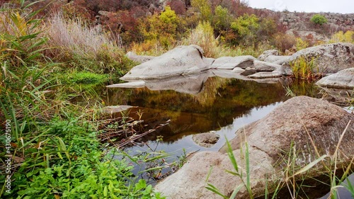 Autumn trees and large stone boulders around. A water cascade in autumn creek with fallen leaves. Water flows around the stones in the river. Aktovsky Canyon, Ukraine. photo