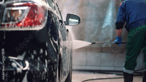 Master in service washes black sedan with in the water and foam with hose rear view