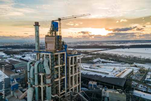 Aerial view of cement plant with high factory structure and tower crane at industrial production area at sunset.