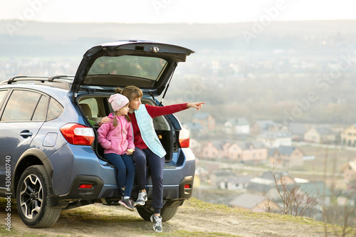Side view of mother with daughter sitting in car trunk and looking on nature. Concept of resting with family on fresh air. © bilanol