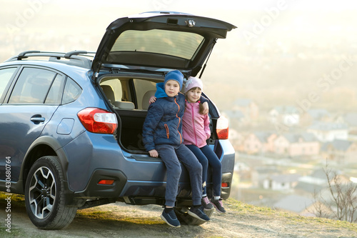 Side view of sister and brother sitting in car trunk and looking on nature. Concept of resting on fresh air with family. © bilanol
