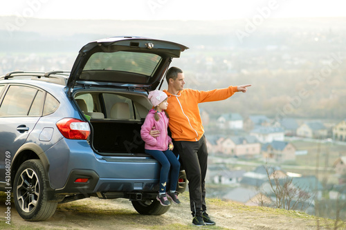 Side view of father with little daughter standing near car with open trunk and enjoying nature. Concept of weekend with family. © bilanol