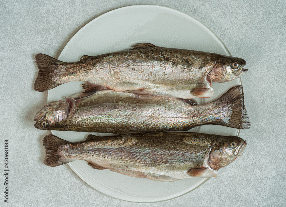 Fresh raw trout fish on a plate.Top view.White marble background.. Fresh raw trout fish on a plate.Top view.White marble background..