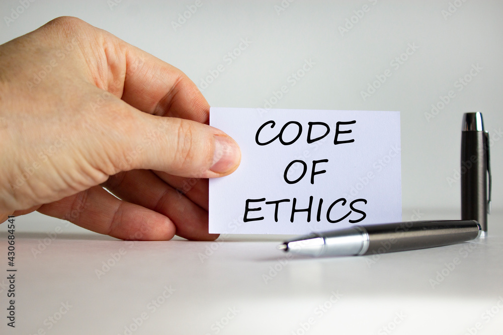 Code of ethics symbol. White paper with words 'Code of ethics' in businessman hand, metalic pen. Beautiful white background. Business and code of ethics concept. Copy space. Code of ethics symbol. White paper with words 'Code of ethics' in businessman hand, metalic pen. Beautiful white background. Business and code of ethics concept. Copy space.