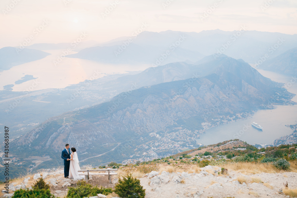 The bride and groom stand holding hands on the observation deck on Mount Lovcen overlooking the Bay of Kotor, top view 