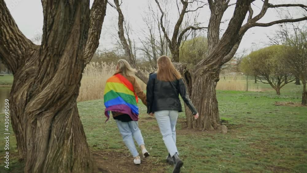LGBT couple wears rainbow flag and runs around tree in park LGBT couple wears rainbow flag and runs around tree in park
