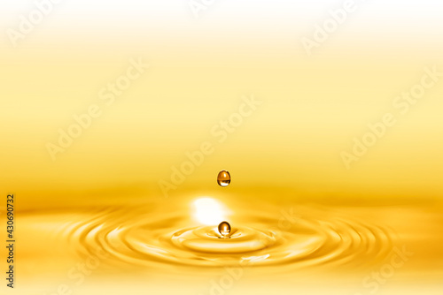 Macro shot of droplets splash of a golden elixir for beauty and body care creating circular waves by falling down on the shining liquid.