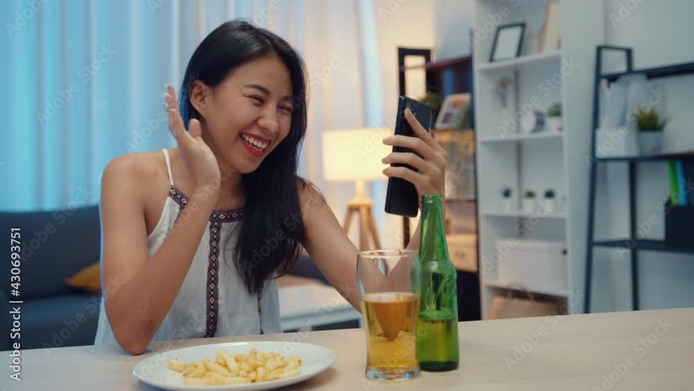 Young Asia lady drinking beer having fun happy moment night party New Year event online celebration via video call by phone at home at night. Social distancing, quarantine for coronavirus prevention. Young Asia lady drinking beer having fun happy moment night party New Year event online celebration via video call by phone at home at night. Social distancing, quarantine for coronavirus prevention.