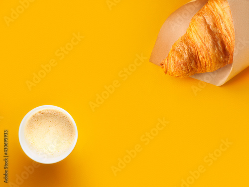 Flat lay of paper cup of coffee and croissant in craft paper on bright orange paper background. Breakfast concept. Minimalism. Copy space.