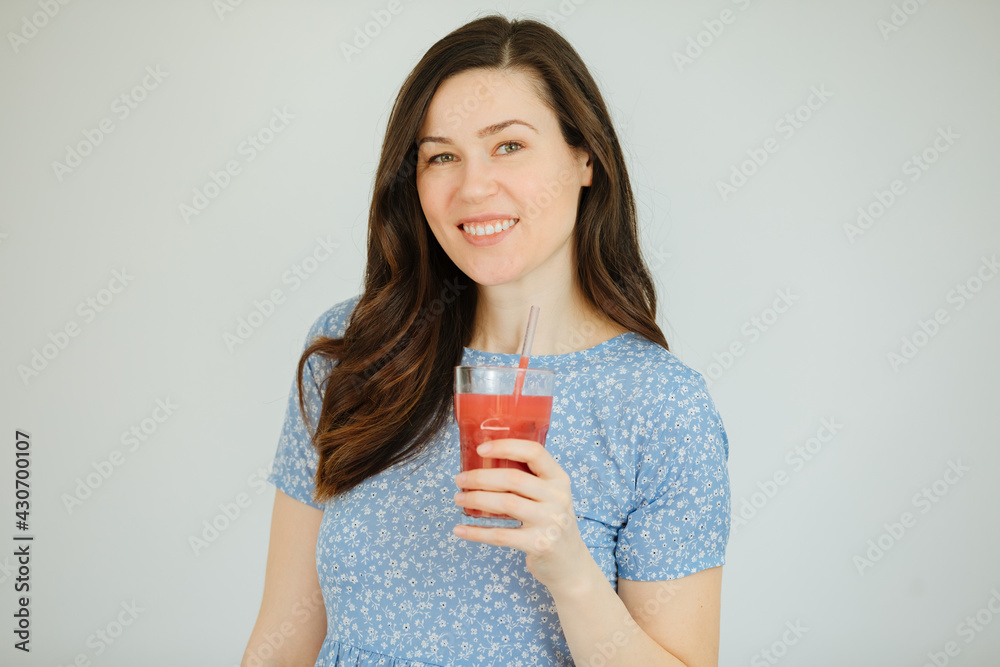 Girl in summer clothes holds a glass with red juice in hand. Beautiful brunette woman drinking a red smoothie. Healthy lifestyle and happiness Girl in summer clothes holds a glass with red juice in hand. Beautiful brunette woman drinking a red smoothie. Healthy lifestyle and happiness
