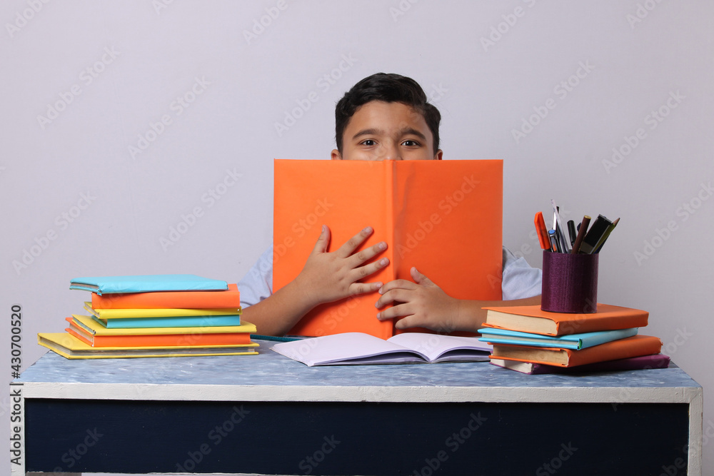 little Indian or asian school boy reading book over study table. stack of books