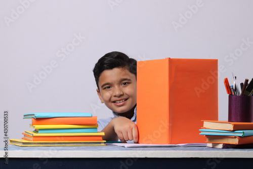 little Indian or asian school boy reading book over study table. stack of books photo