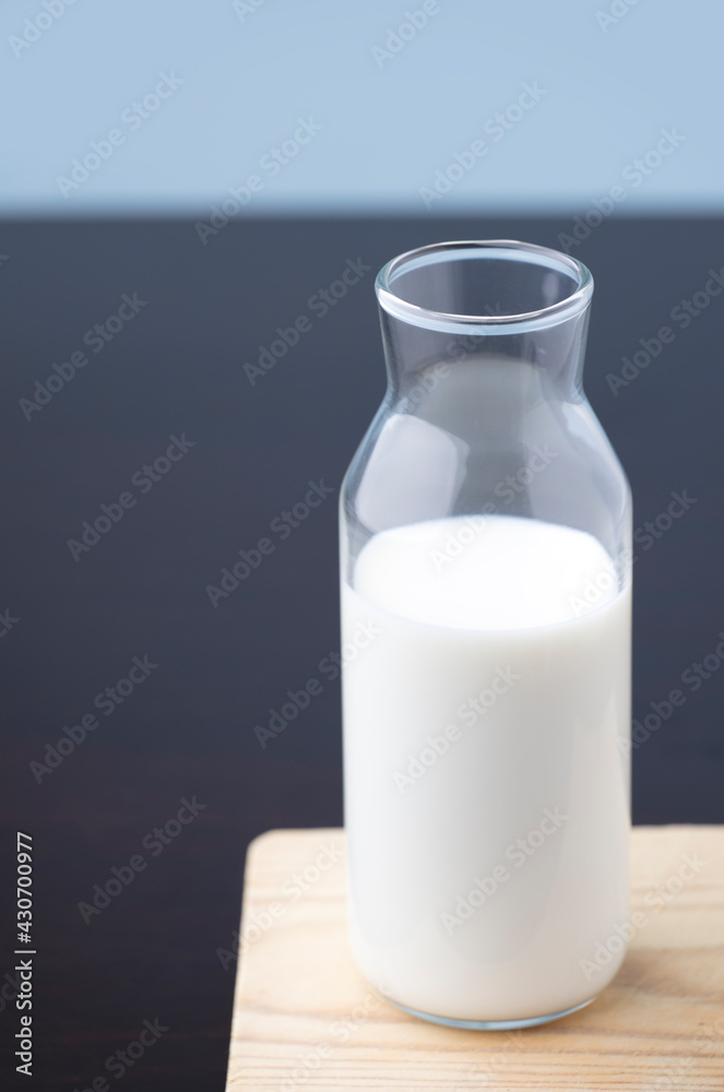 transparent glass milk bottle, on wood, blue background transparent glass milk bottle, on wood, blue background