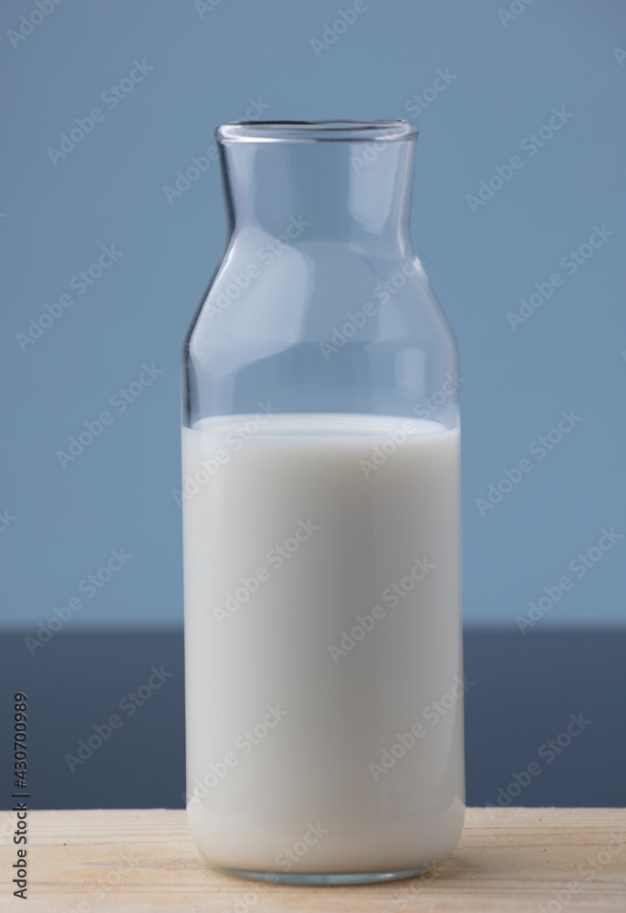 transparent glass milk bottle, on wood, blue background transparent glass milk bottle, on wood, blue background