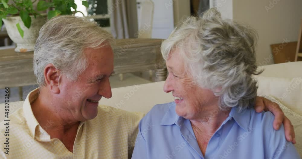 Caucasian senior couple smiling while looking at each other sitting on the couch at home Caucasian senior couple smiling while looking at each other sitting on the couch at home