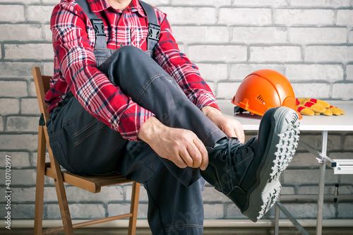  Worker putting on working boots at the locker room in a factory. Safety construction concept.