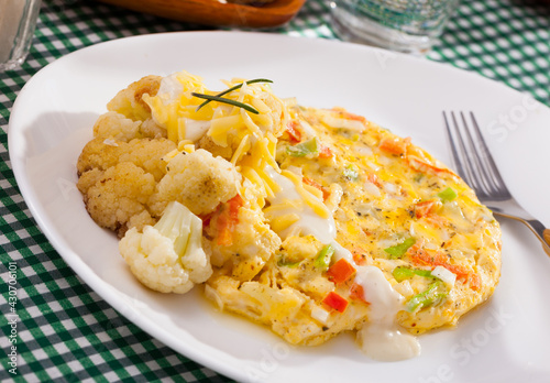 Delicious vegetable omelette served on white plate with cauliflowers, grated cheese and cream sauce..