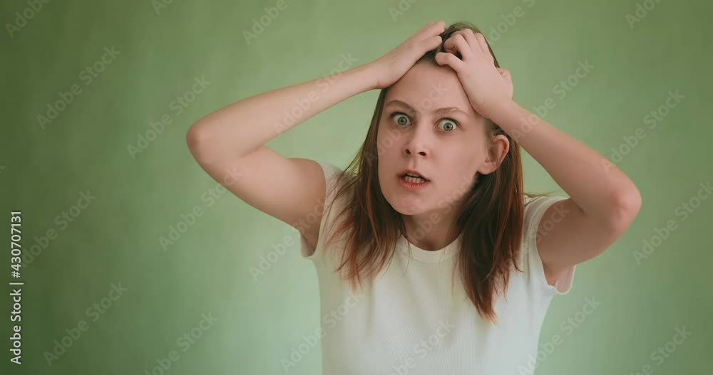 Emotional angry young woman in white t-shirt clutches head and pulls hair demonstrating despair to camera on green slow motion Emotional angry young woman in white t-shirt clutches head and pulls hair demonstrating despair to camera on green slow motion