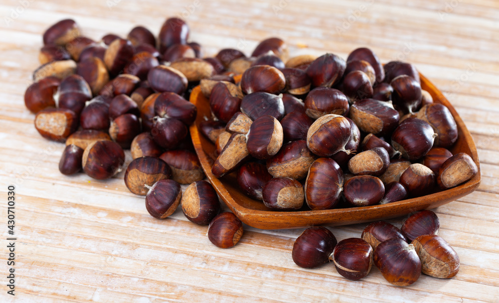 Obraz premium Pile of raw edible chestnuts in wooden bowl on table. Cooking of popular street food