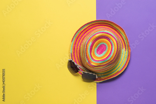 Top view of a colorful summer hat with glasses on a yellow and purple background.