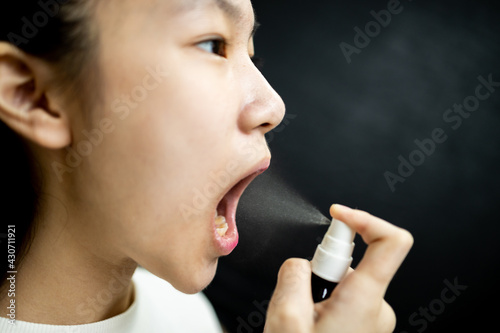Фотография Asian child girl spraying medicine,treatment for pain in oral,sore throat with c