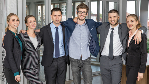 Group portrait of six business people team standing together in an office and cuddle around necks together with smile faces and self-confidence. Idea for success of teamwork in modern business