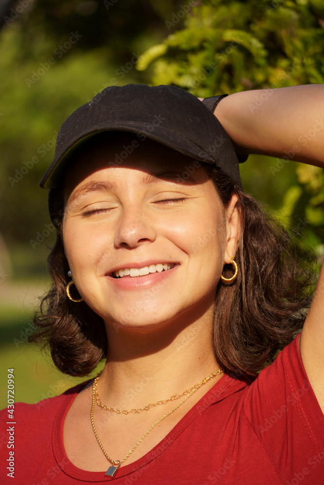 Young girl in black cap and red t-shirt in the park at sunset. Sunny day and open countryside with lots of nature while she feels the sunlight. Young girl in black cap and red t-shirt in the park at sunset. Sunny day and open countryside with lots of nature while she feels the sunlight.