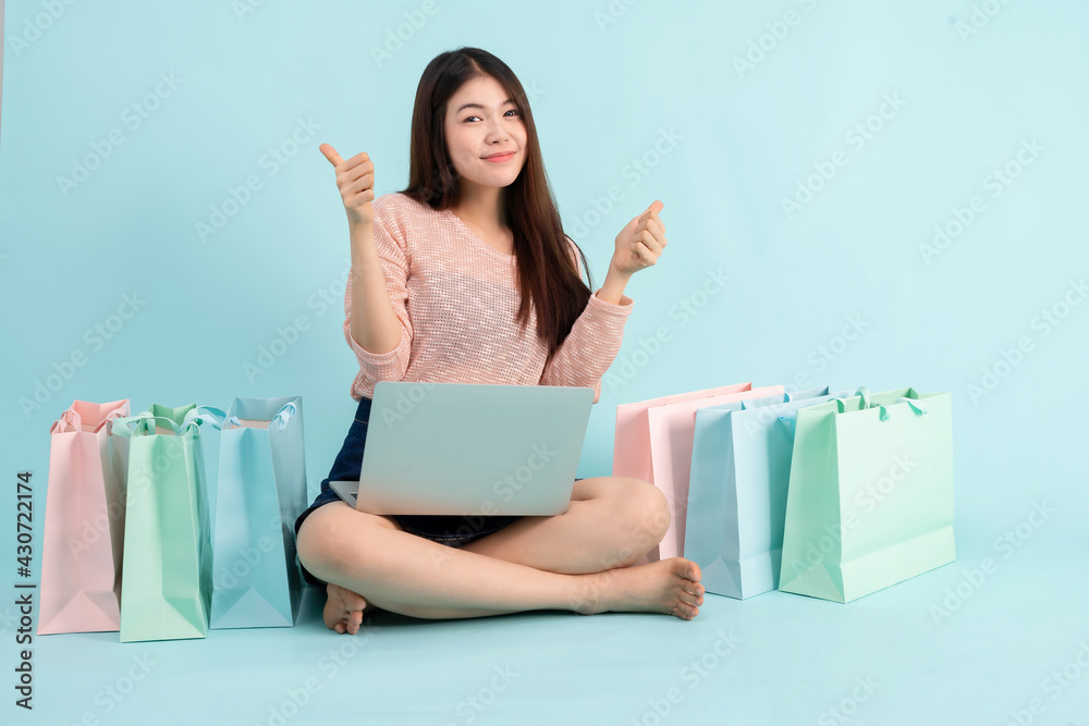 Online Order. Asian girl sitting with laptop using credit card shopping online on blue background, shopping online concept Online Order. Asian girl sitting with laptop using credit card shopping online on blue background, shopping online concept