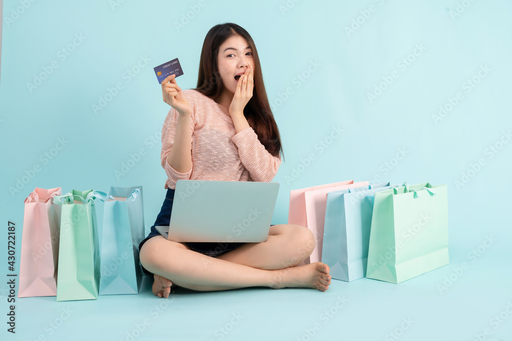 Online Order. Asian girl sitting with laptop using credit card shopping online on blue background, shopping online concept Online Order. Asian girl sitting with laptop using credit card shopping online on blue background, shopping online concept