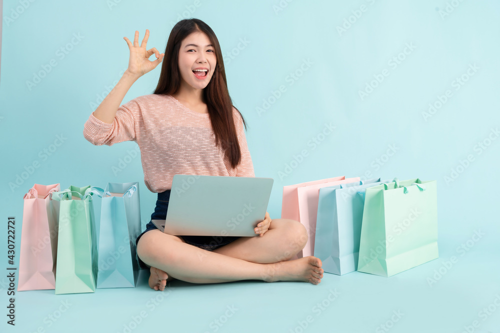 Online Order. Asian girl sitting with laptop using credit card shopping online on blue background, shopping online concept Online Order. Asian girl sitting with laptop using credit card shopping online on blue background, shopping online concept