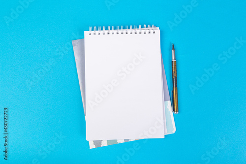stack of school exercise books on blue background, spiral notepad with blank page and pen on table top view