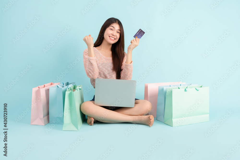 Online Order. Asian girl sitting with smart phone using credit card shopping online on blue background, shopping online concept
